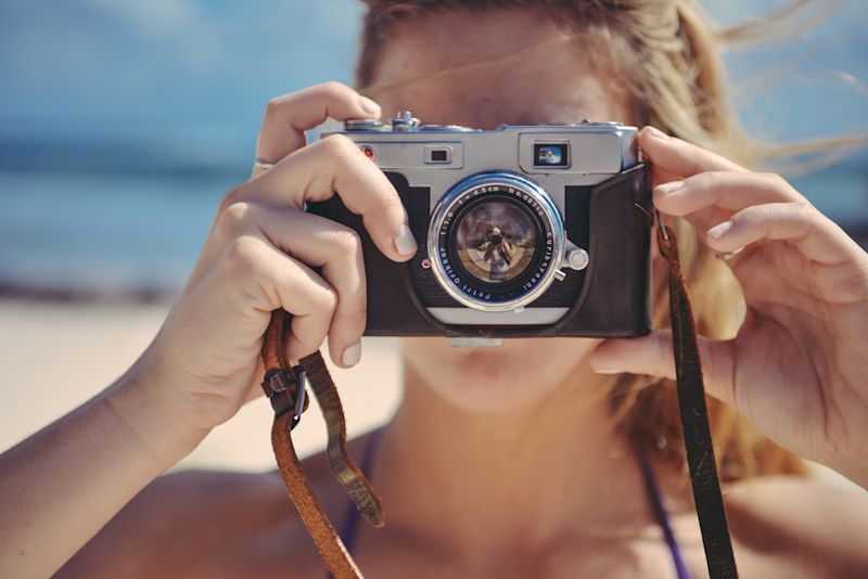 Blonde girl looking into camera holding up a camera