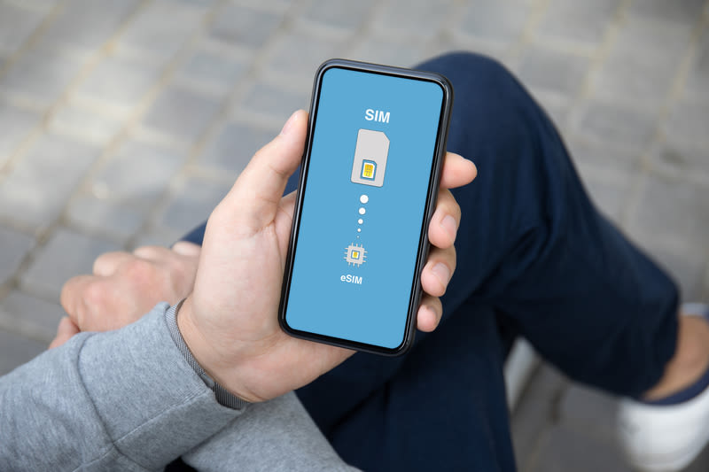 eSIM on mobile phone held in hand of man seated on a street