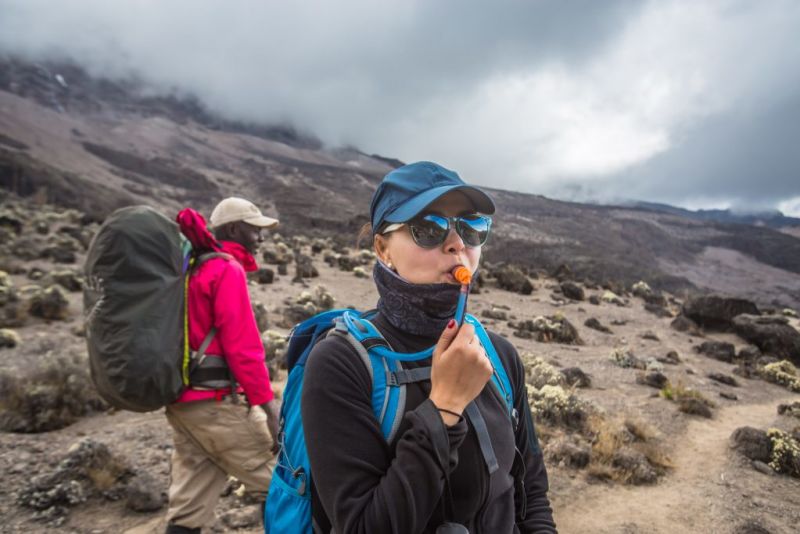 A lady drinking water on Mount Kilimanjaro to help ease altitude sickness