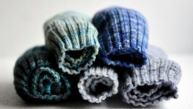Close up of five pairs of woollen socks rolled up and placed in a neat pile on a white table