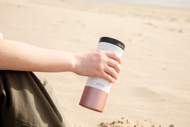 woman holding travel mug on beach, sustainable packing list eco-friendly environmental