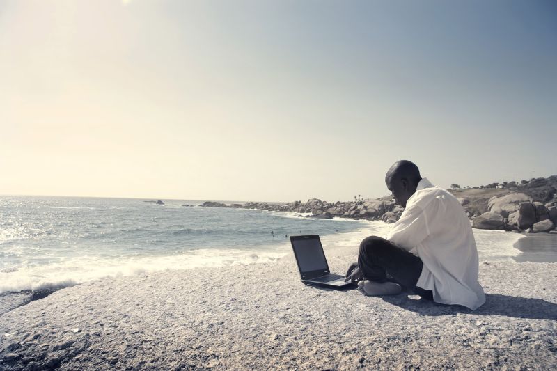 Man sitting on beach and working on laptop