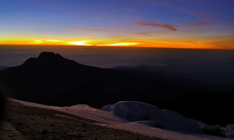 View of the sunrise over a cloudbank as seen from the summit of Kilimanjaro with a glacier in the foreground