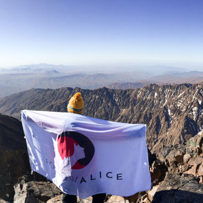 Client stands with Follow Alice flag on mountain