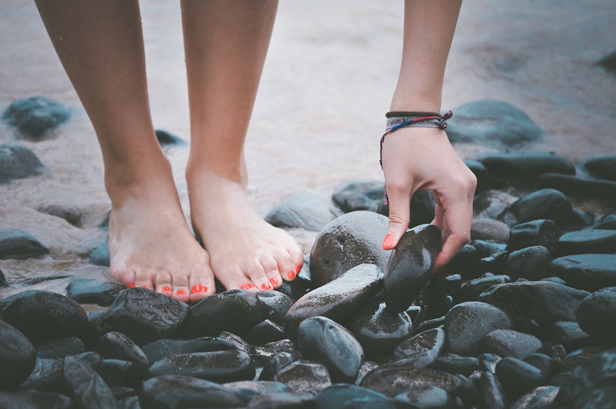 Woman painted nails standing on sand, stones, beach