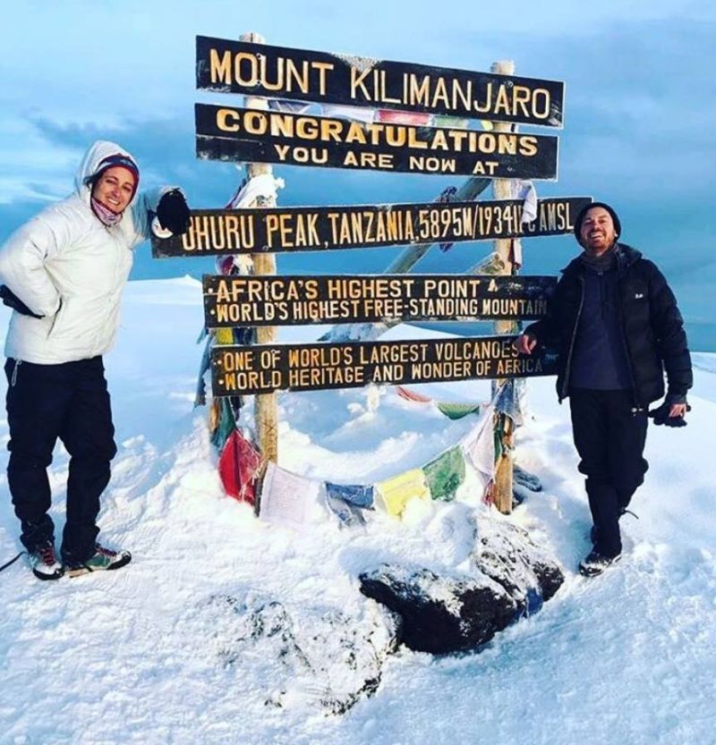Two trekkers smiling by Uhuru Peak on a very snow-covered Kilimanjaro summit