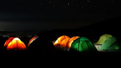 Starry sky over Kilimanjaro campsite with orange and green dome tents lit up from within
