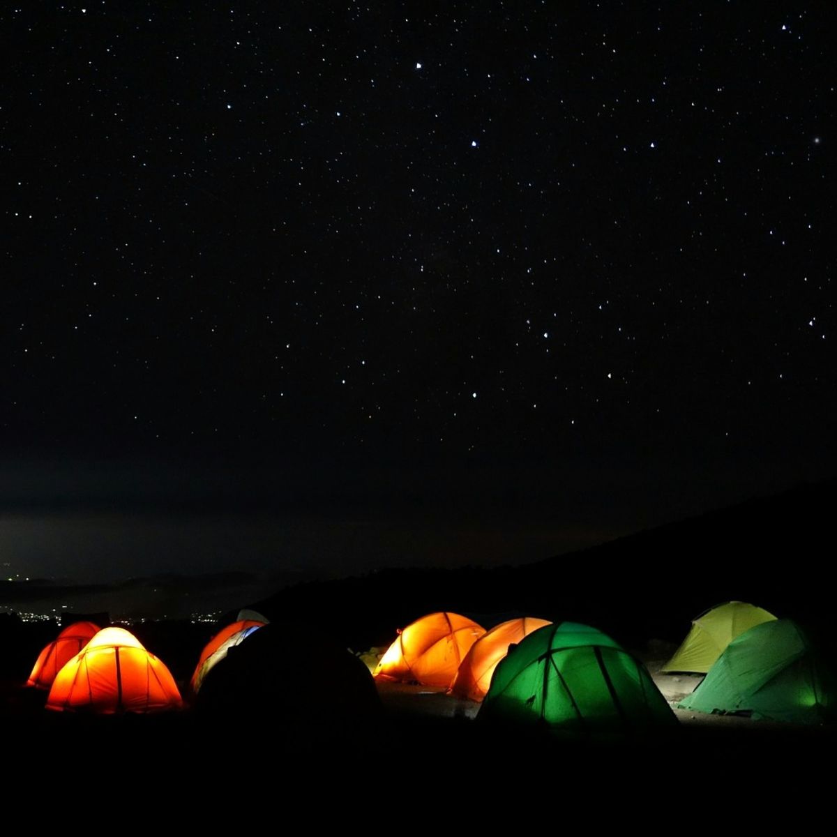 Starry sky over Kilimanjaro campsite with orange and green dome tents lit up from within