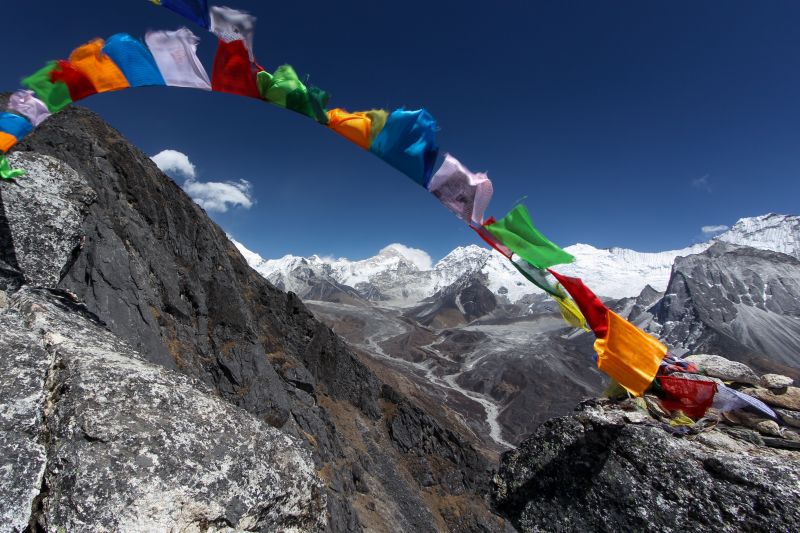 A view taken from high about over a valley along the Everest Base Camp route and with Tibetan prayer flags blowing wildly in the wind in the foreground