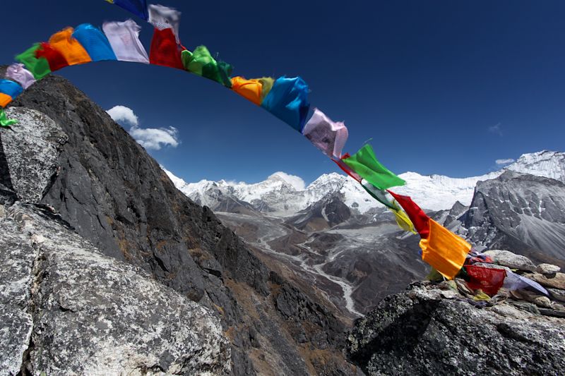 A view taken from high about over a valley along the Everest Base Camp route and with Tibetan prayer flags blowing wildly in the wind in the foreground