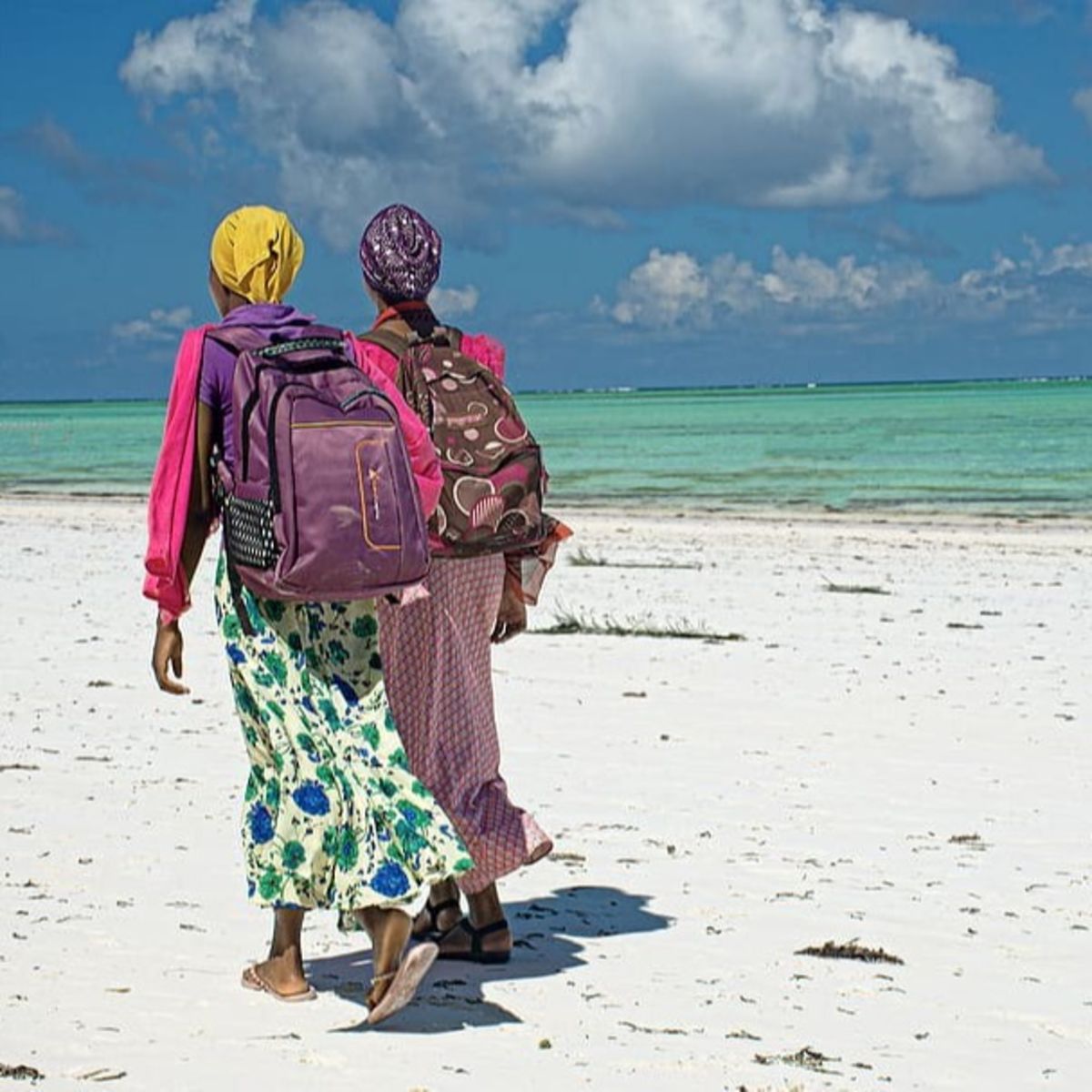 Women wearing backpacks walking along the beach in Zanzibar