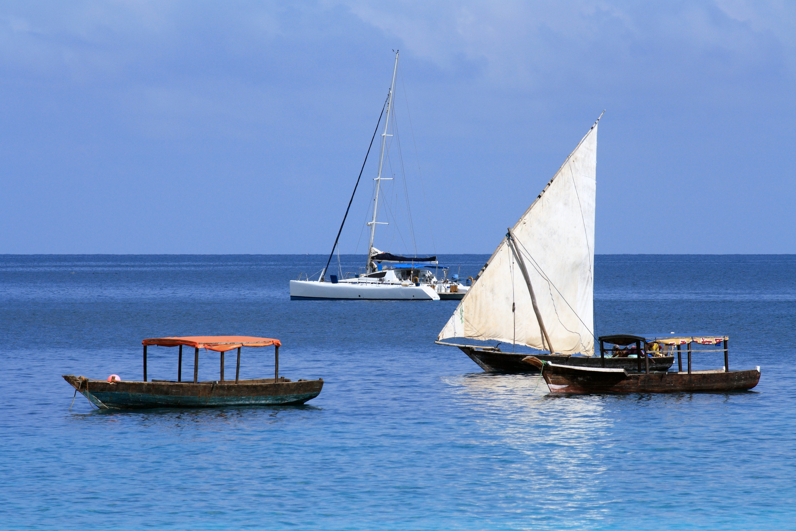 Old boats (dhow and other) and modern boat (catamaran) in Zanzibar on a sunny day