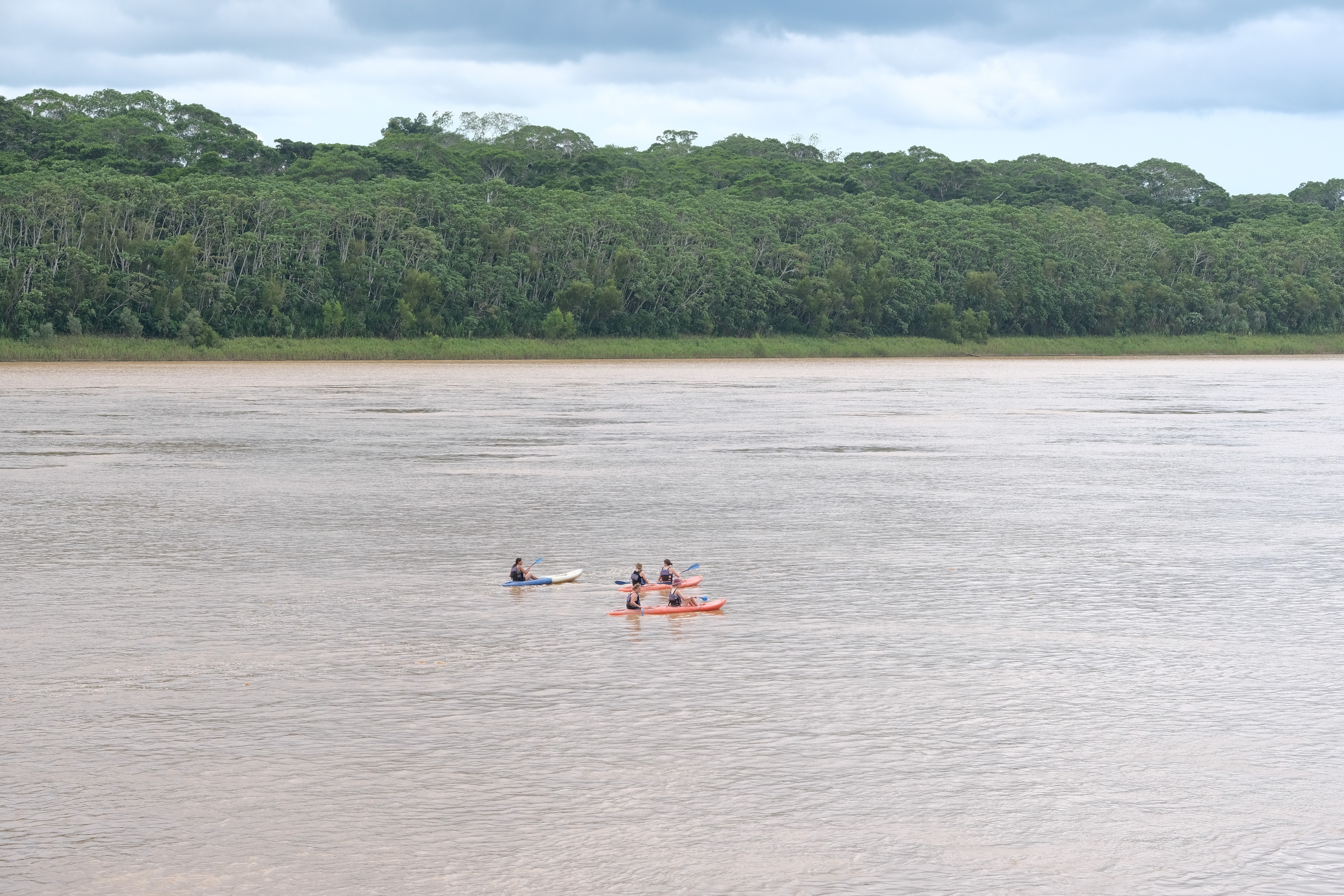 People canoeing kayaking on Amazon river with green jungle tree and sky at Puerto Maldonado Peru.