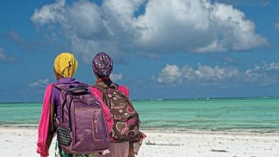 Women wearing backpacks walking along the beach in Zanzibar