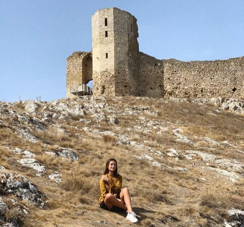 Young woman sitting on grass near ruin 