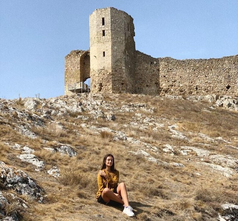 Young woman sitting on grass near ruin