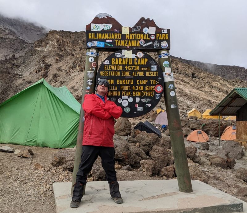 Man in red jacket standing by Barafu Camp sign on Kilimanjaro, Tanzania