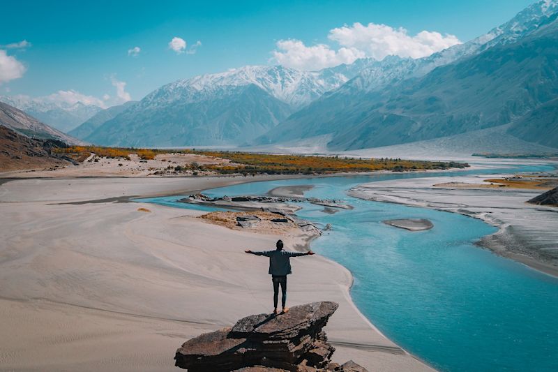 Man standing on a rock in a valley with mountains and a river