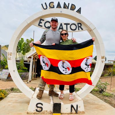 Couple smiling and holding Ugandan flag by Equator sign