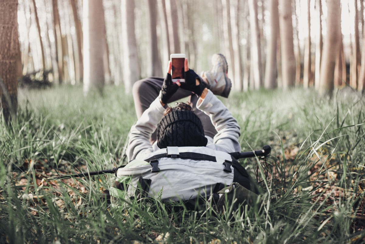 Hiker lying down with backpack and looking at phone