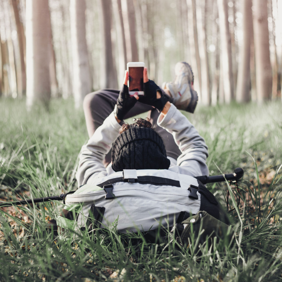 Hiker lying down with backpack and looking at phone