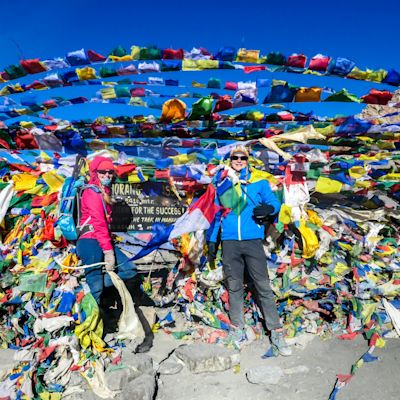 A couple standing between prayer flags at the top of Thorung La Pass, Annapurna Circuit Trek, Nepal