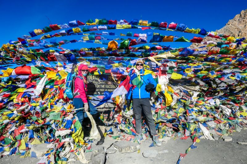 A couple standing between prayer flags at the top of Thorung La Pass, Annapurna Circuit Trek, Nepal 