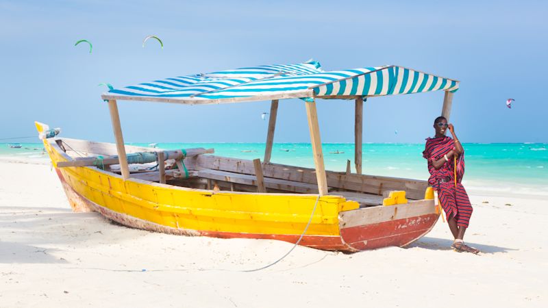 Maasai warrior lounging around on traditional colourful wooden boat on picture perfect tropical sandy beach on Zanzibar, Tanzania, East Africa. Kiteboarding spot on Paje beach.