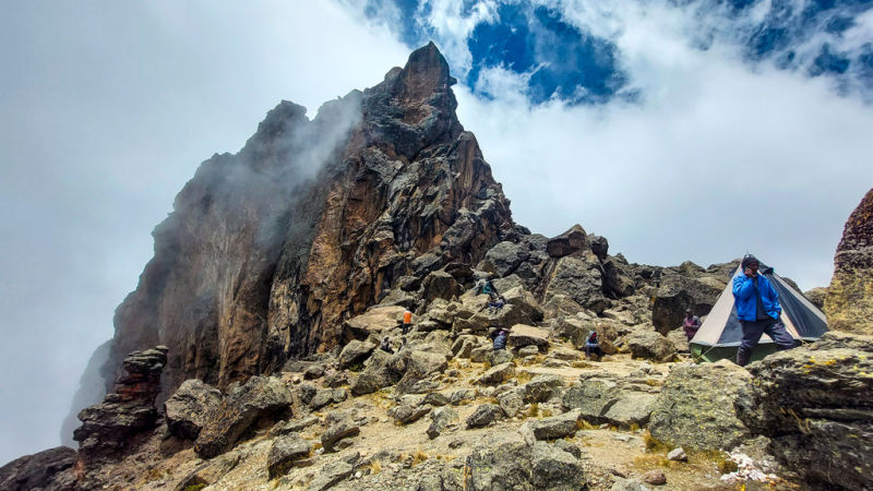 View of Lava Tower with tent and climber in blue jacket on Kilimanjaro climb, Machame and Lemosho routes