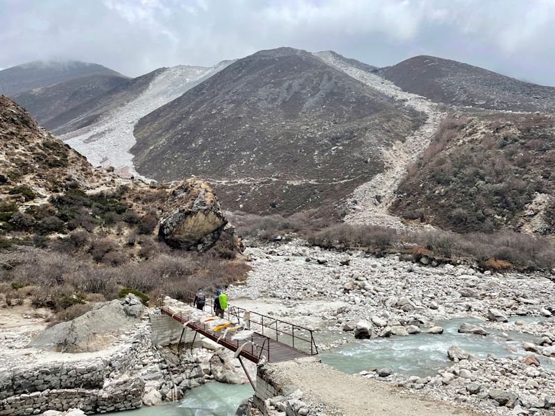 EBC trekker on small bridge crossing a stream among snow and ice, Antonia and Dennis pic