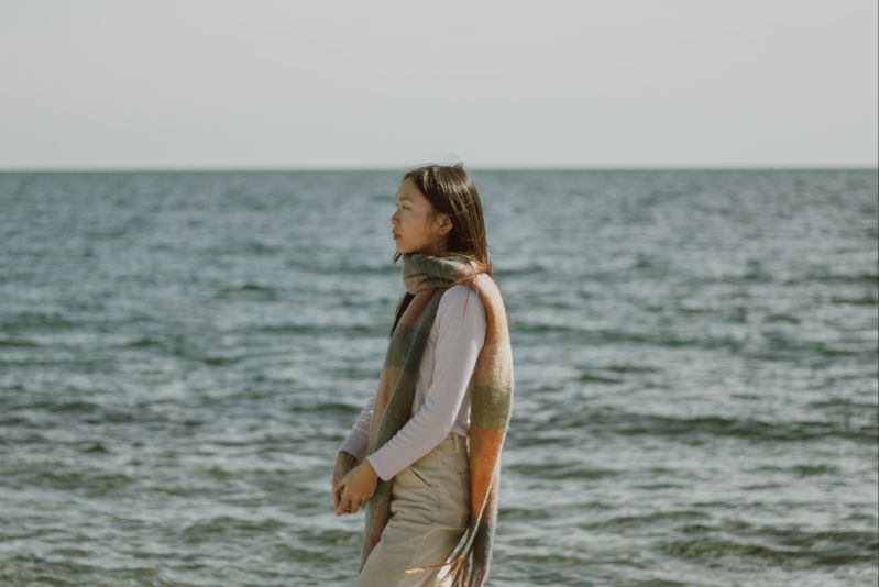 Young woman in warm clothes looking pensive by ocean