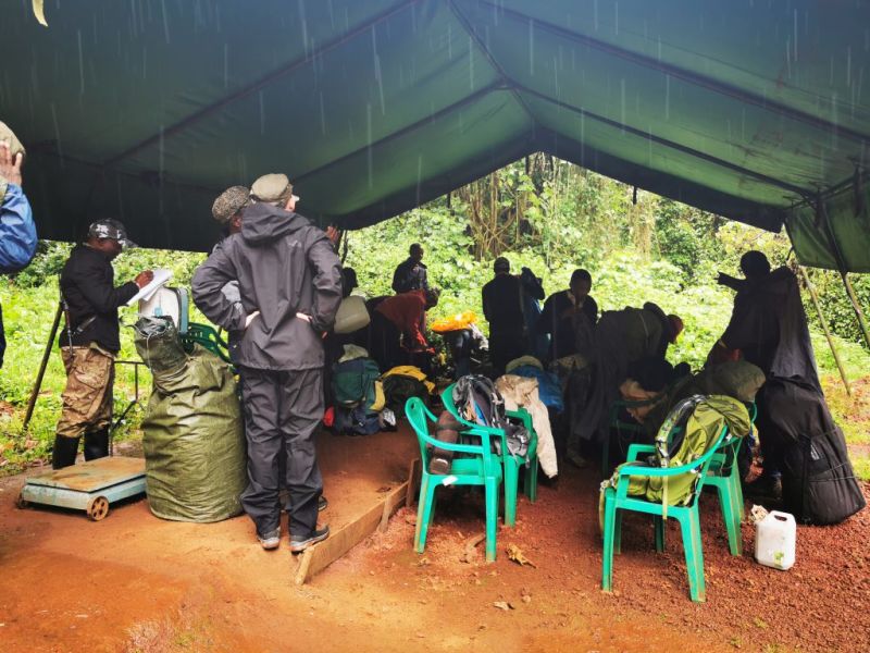 Men standing under a tarp in the rain organising trekking equipment