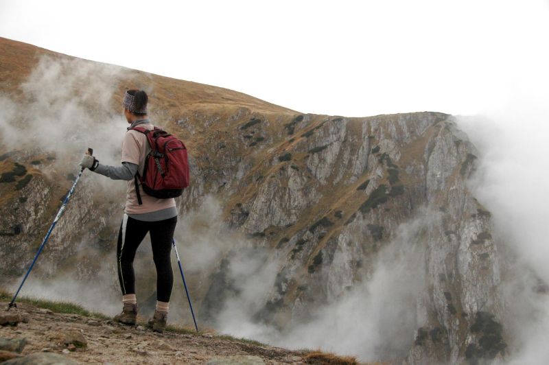 Woman trekker with backpack and trekking poles in misty, dry mountains