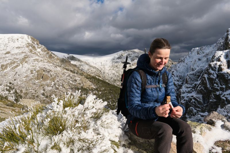 Glad female backpacker/hiker eating snack while sitting on snowy mountain